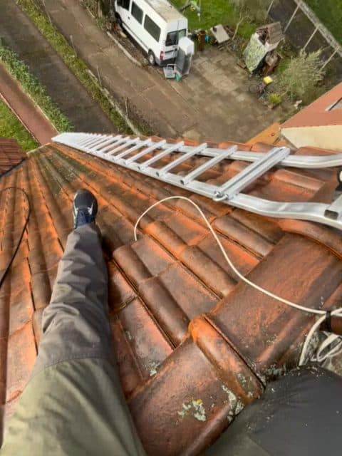Vue depuis une toiture en tuiles avec échelle de couvreur crochetée sur le versant, descendant vers la gouttière et la rue en contrebas