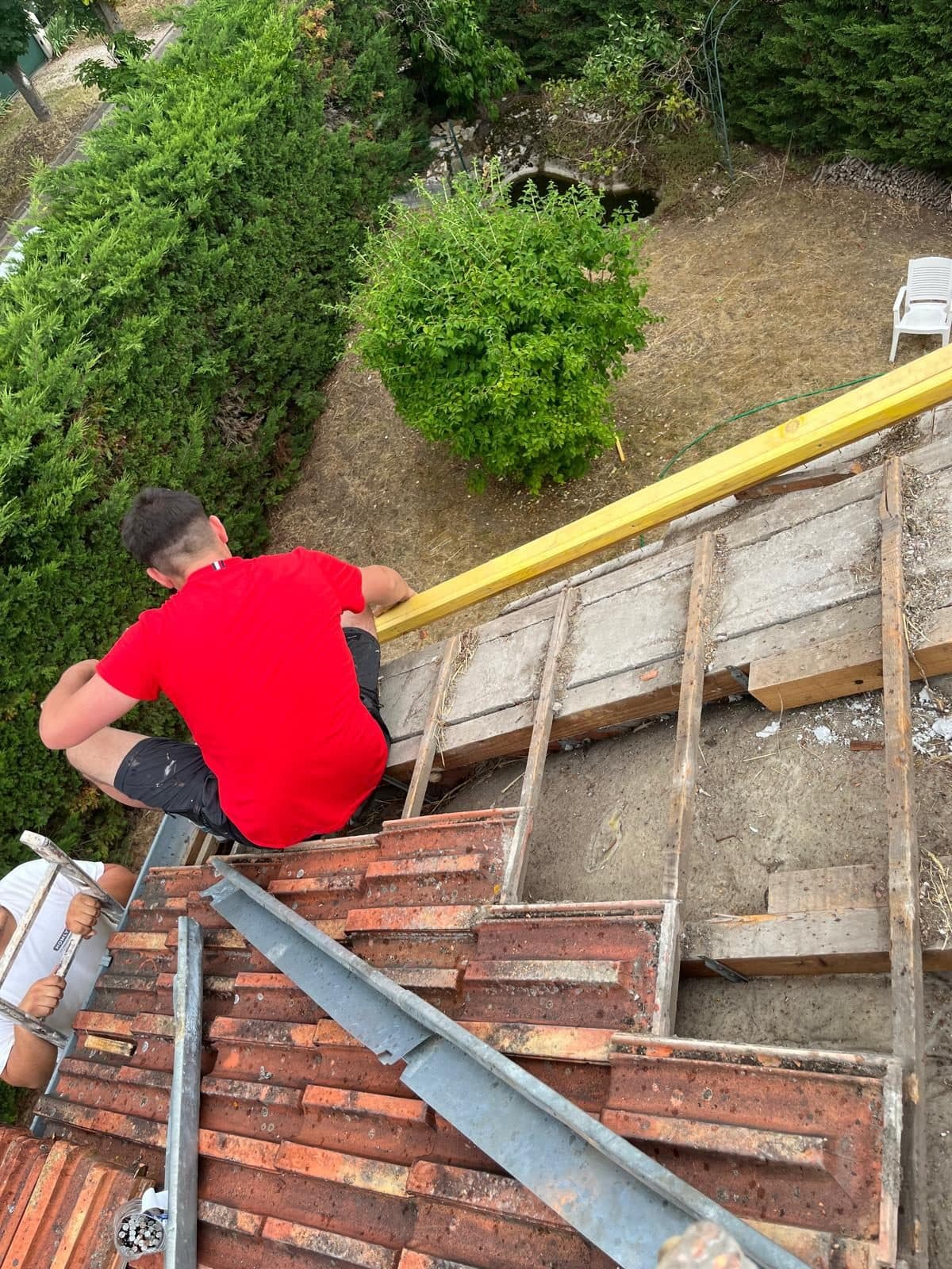 Deux couvreurs déposant l'ancienne couverture en tuiles d'une maison, mettant à nu les voliges et posant un liteau neuf