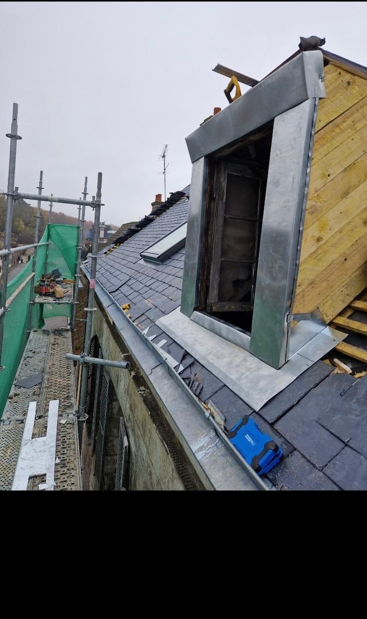 Lucarne en cours de reprise sur une toiture en ardoise, avec habillage neuf en zinc sur les joues et le fronton, vue depuis l'échafaudage