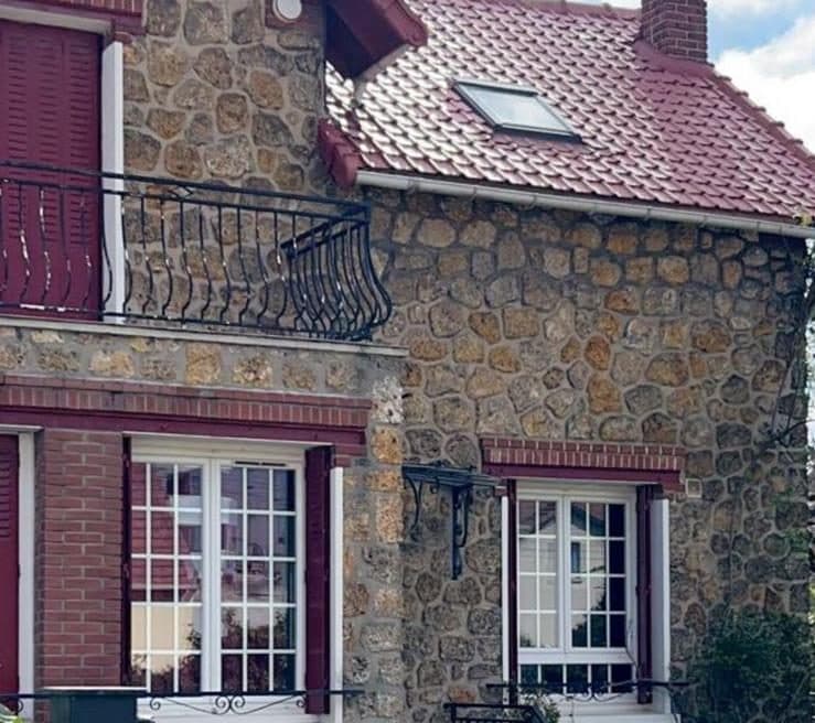 Fenêtre de toit posée sur la couverture en tuiles d'une maison en pierre meulière, avec gouttière et descente le long de la façade