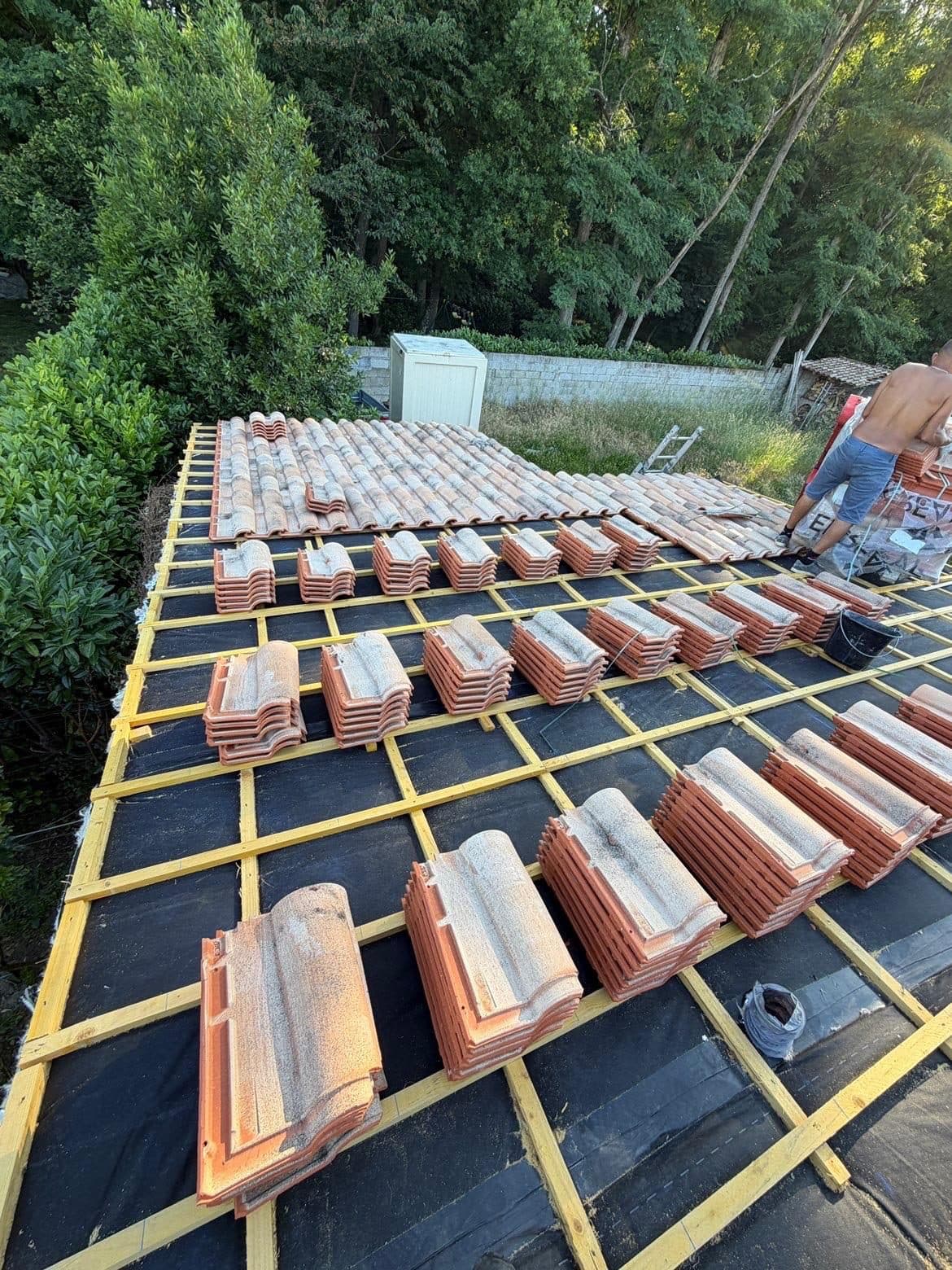 Couvreur posant des tuiles neuves réparties par piles sur le liteaunage d'une toiture en cours de réfection, sur écran de sous-toiture noir