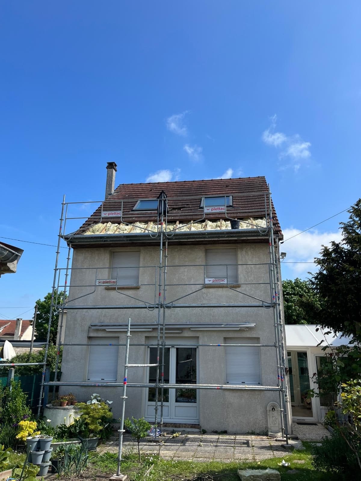 Maison sous échafaudage dont la toiture est ouverte en partie basse, laissant voir l'isolant en place entre les chevrons, avec deux fenêtres de toit