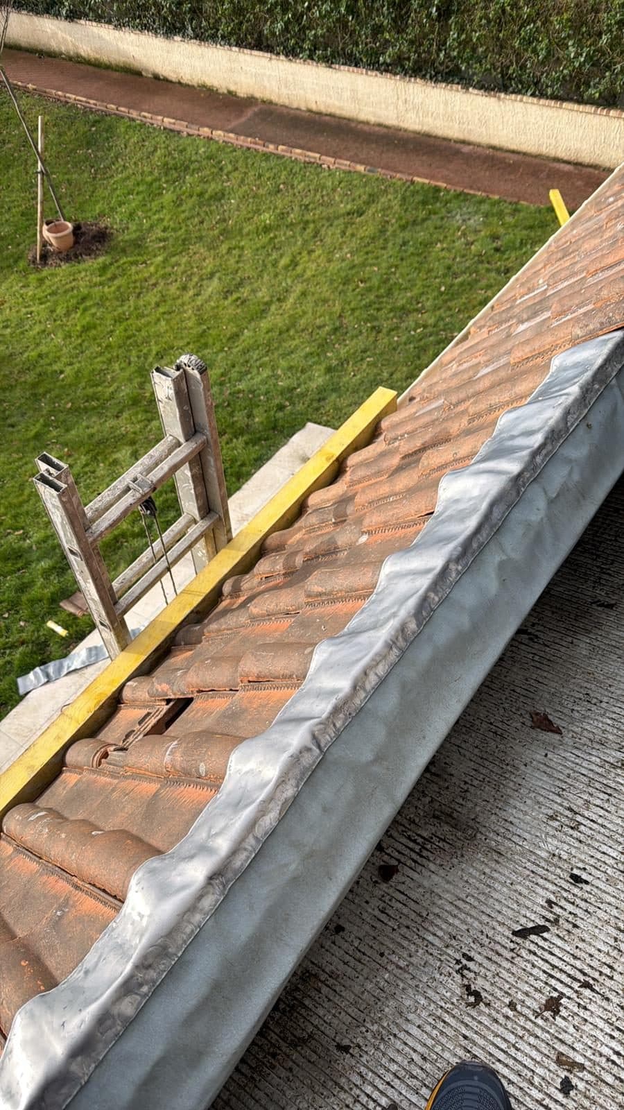 Solin en zinc neuf façonné à la main le long d'une toiture en tuiles, assurant l'étanchéité entre la couverture et le mur